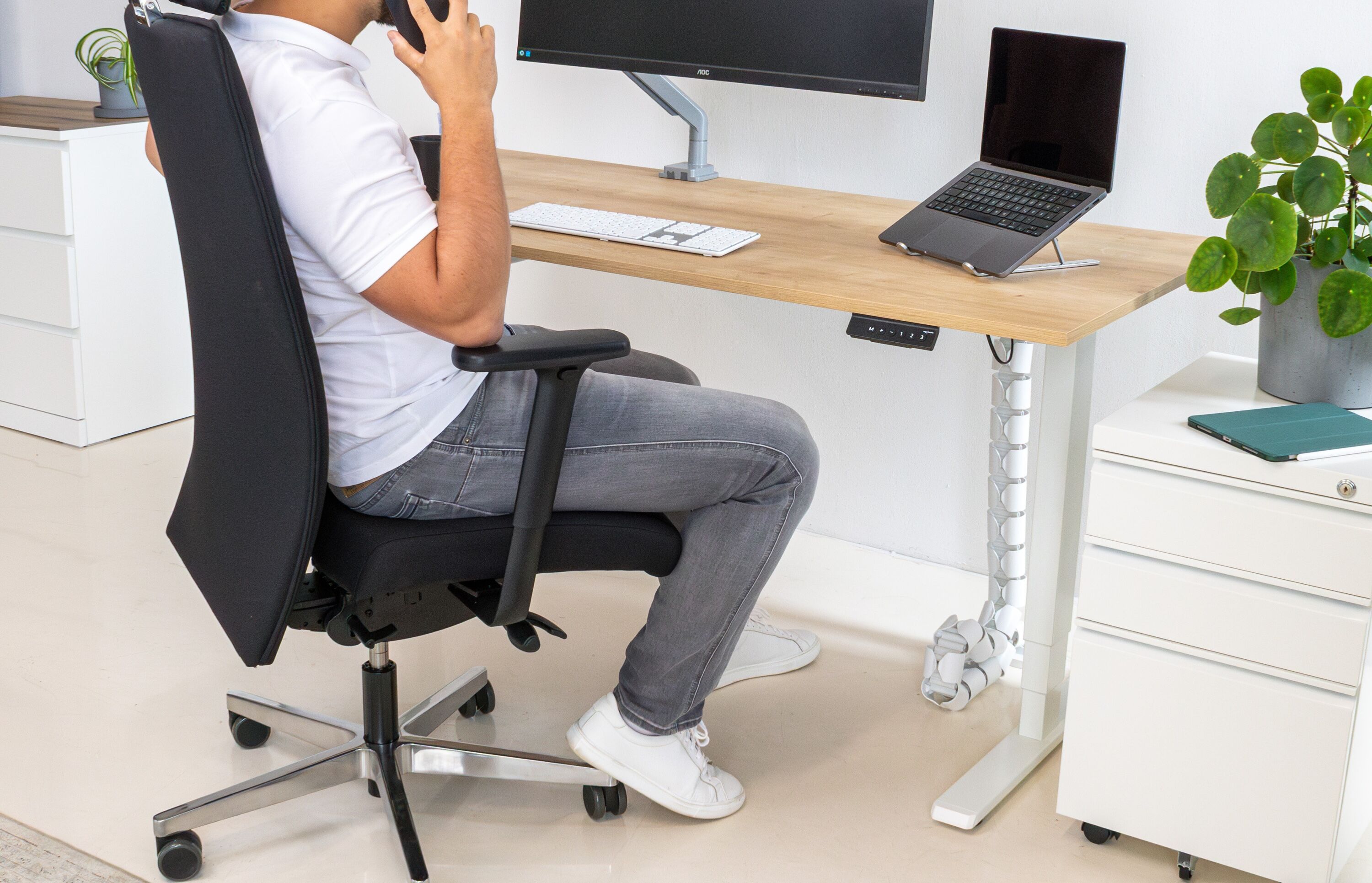 Ein Mann sitzt an seinem höhenverstellbaren Schreibtisch und telefoniert.