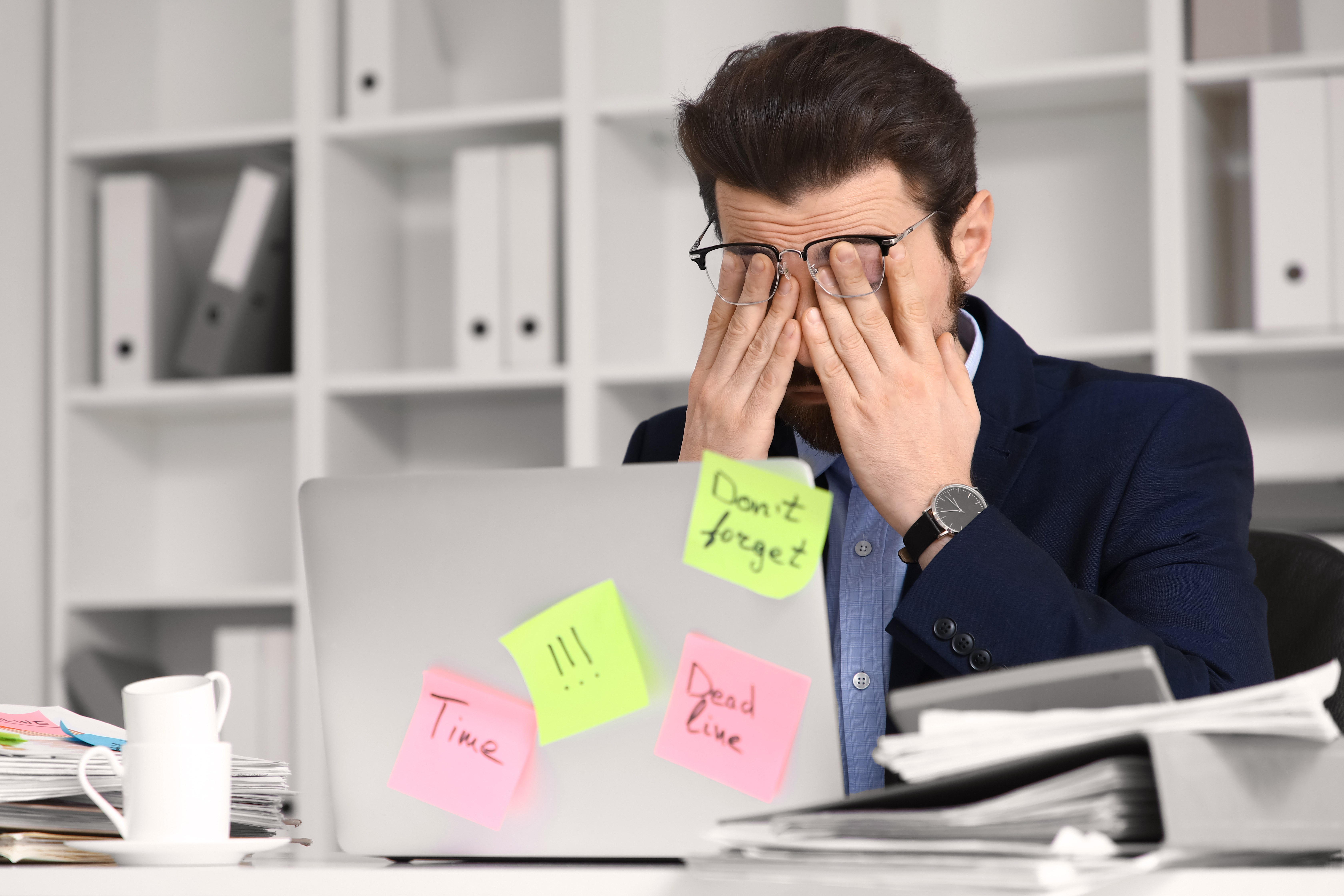 Gestresster Mann reibt sich die Augen vor dem Laptop – müde bei der Arbeit unter Zeitdruck